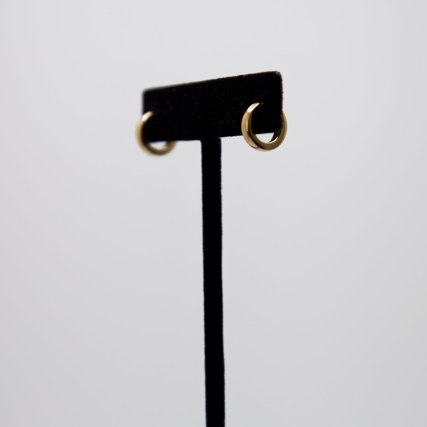 14k Gold Mini Hoop Earrings on a black earring stand.